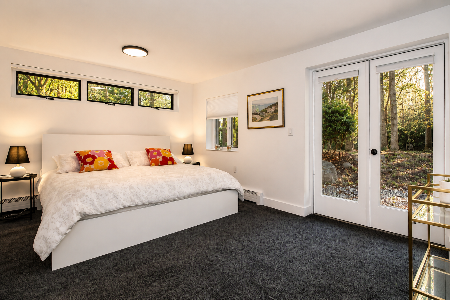Primary suite with a white platform bed, garden views through glass doors, and warm afternoon light.