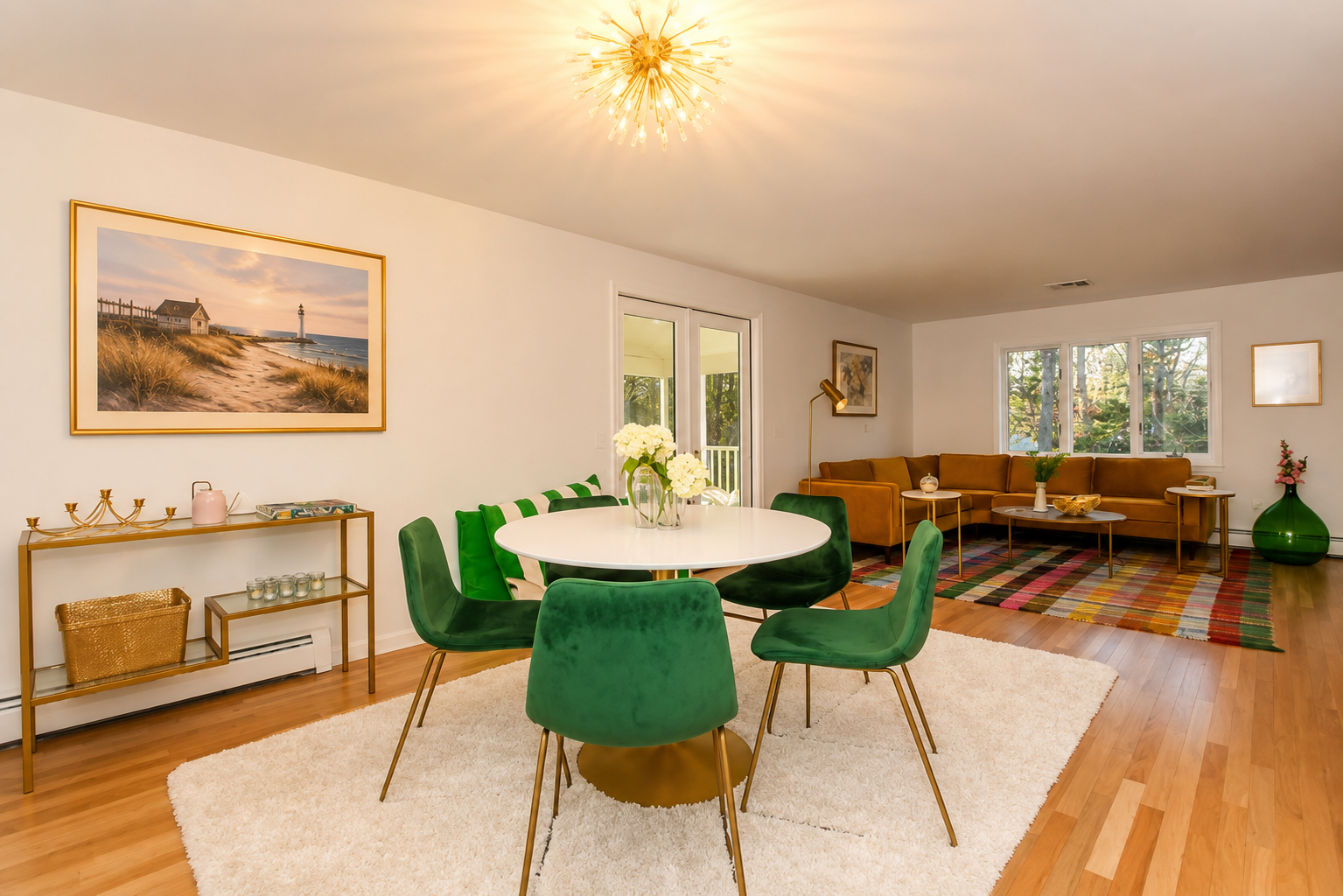Sun-filled great room with a white dining table, emerald velvet chairs, a brass sputnik chandelier, and a warm living area beyond.